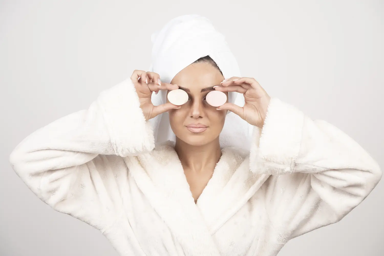 Une femme relaxée dans un peignoir blanc, appliquant un masque visage dans le cadre de sa routine spa à la maison MIHI.